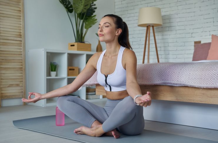 Attractive young woman in sports clothing meditating at home